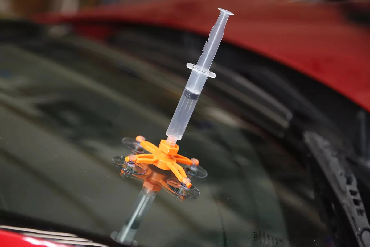 A syringe with its plunger pulled up sits inside the repair jig of a windshield repair kit.