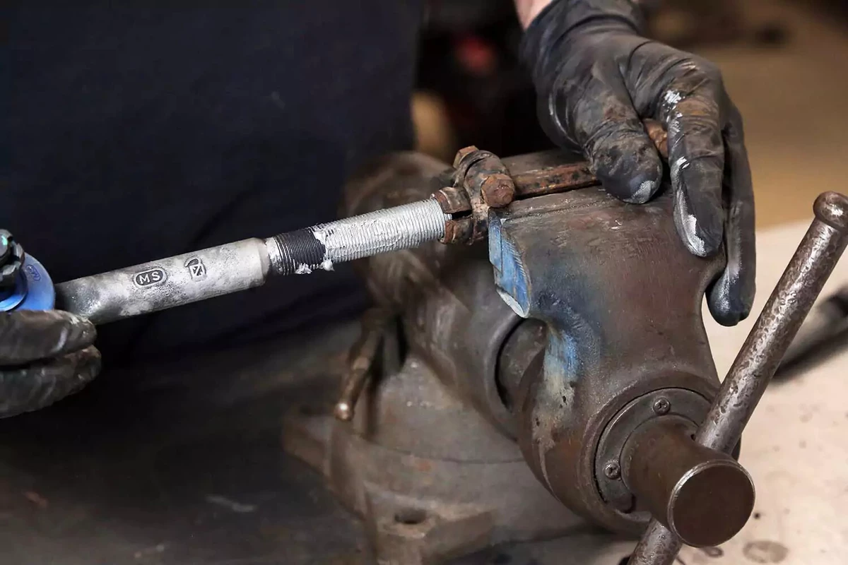 A mechanic screws a tie rod end into its sleeve, after coating it with anti-seize compound.