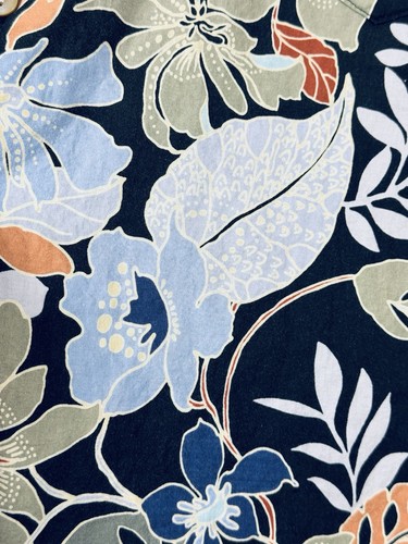 Navy blue Hawaiian shirt with white floral print, green leaves, and orange accents on a wood surface.