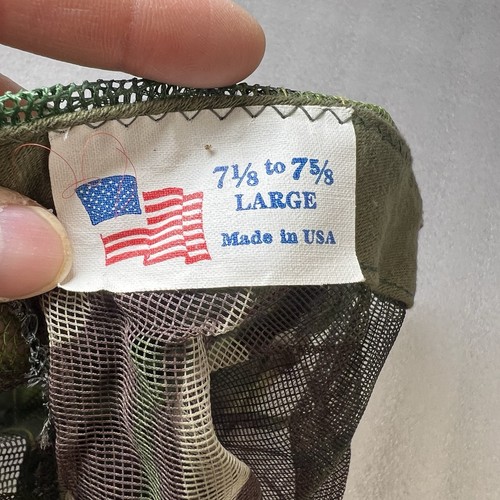 Close-up of Vtg Camo hunting mosquito net facemask with green and red camo pattern and white fabric label reading “7½ to 75% LARGE MADE IN USA.”