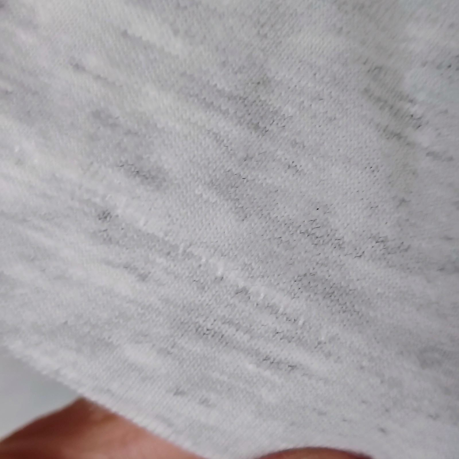 Close-up of worn white fabric with faint gray surface stain, small dark spot on left sleeve, and visible stitching.