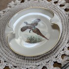 Lenox porcelain ashtray with gold rim, pheasant and brown background, three cigarette rests on woven mat.
