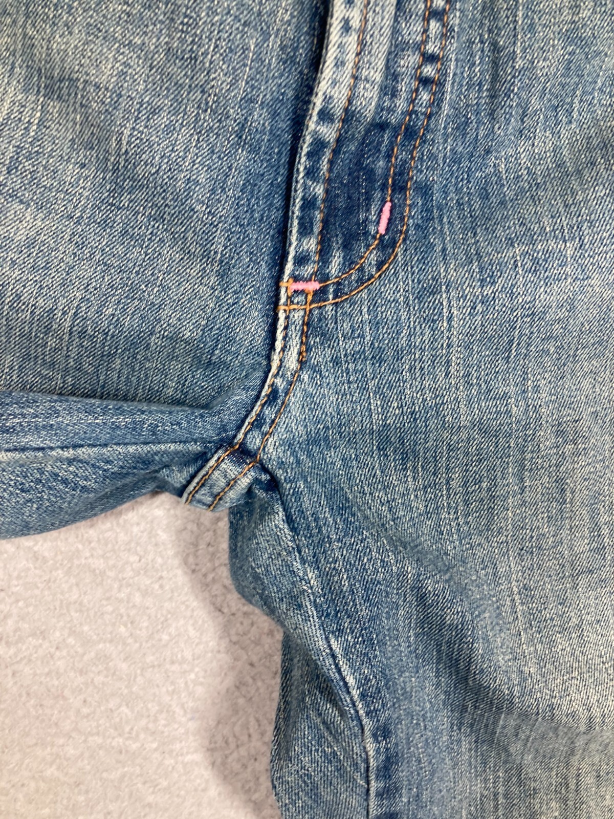 Light blue Karen Kane Lifestyle jeans with pink stitching and double button closure, rolled on a beige surface.