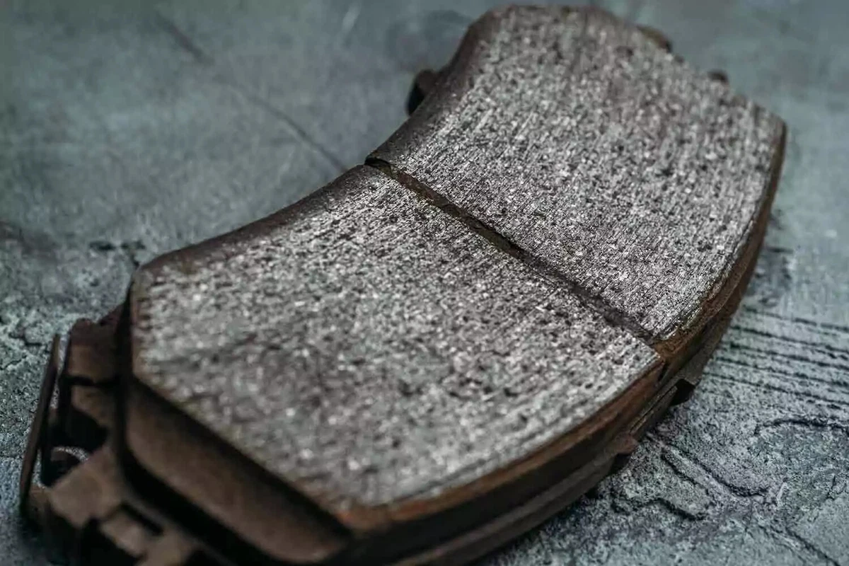A worn-out brake pad is displayed on a dark concrete surface.