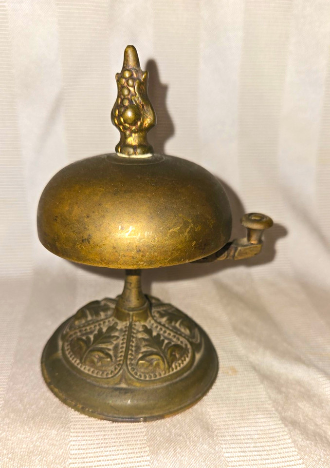 An ornate Victorian brass desk bell with a carved floral base — ring it to summon your assistant, your cat, or just your own sense of self-importance.