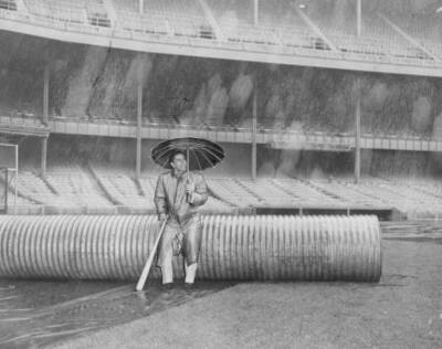 Yankees shortstop Phil Rizzuto sits under umbrella in the rain at  .. Old Photo