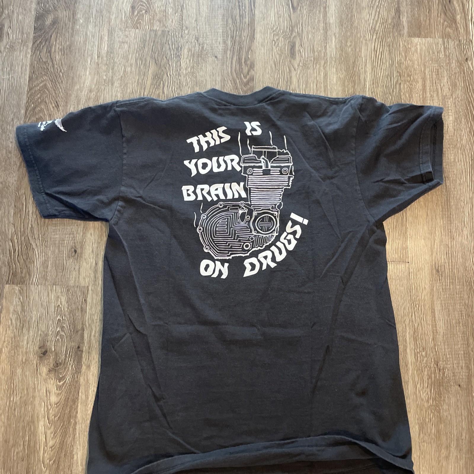 Black short-sleeve shirt with white text reading “VTG 90s LEE THIS IS YOUR BRAIN ON DRUGS!” and motorcycle graphic on back.