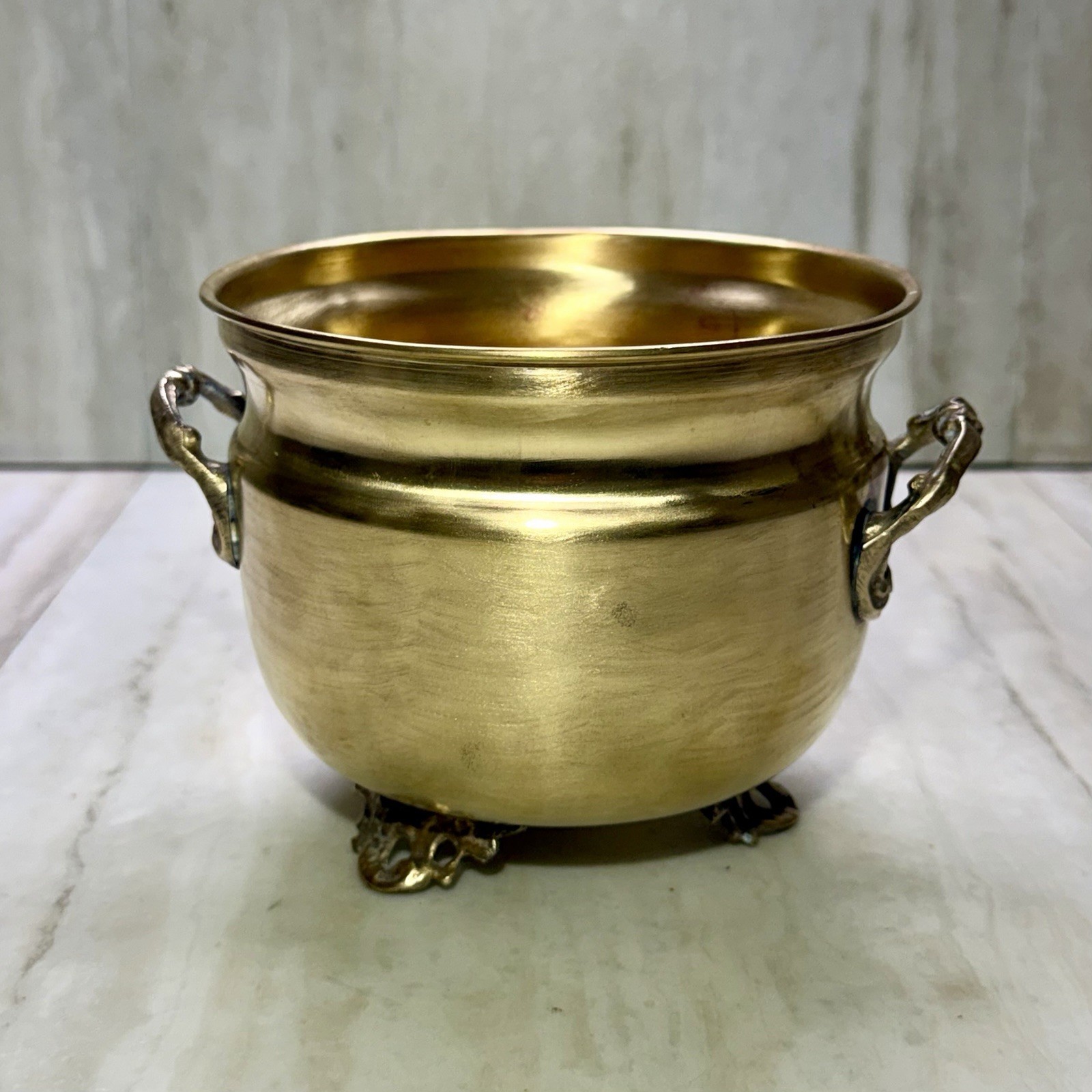Footed brass planter with scroll handles on a white background.