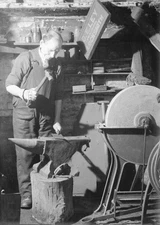 Blacksmith works in his forge hammering out a metal sheet on his a- Old Photo