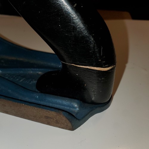 Close-up of worn black metal hand plane with visible scratches and smooth curved handle against white background.
