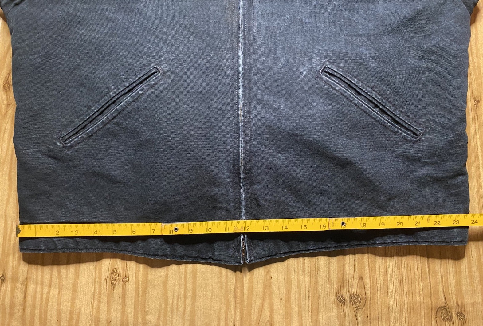 Black Carhartt J01 BLK Detroit jacket with two front zipper pockets and yellow measuring tape across the back.