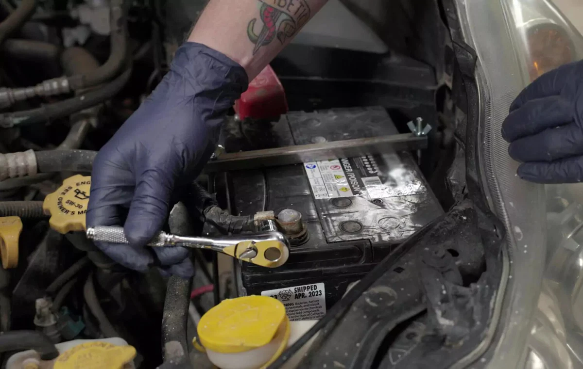 Removing a car battery’s negative clamp with a socket wrench.