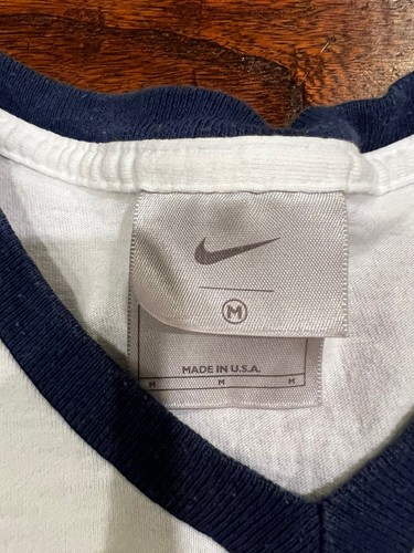 White Nike T-shirt size M with navy trim, featuring red swoosh logo and “MADE IN USA” text on white fabric tag.