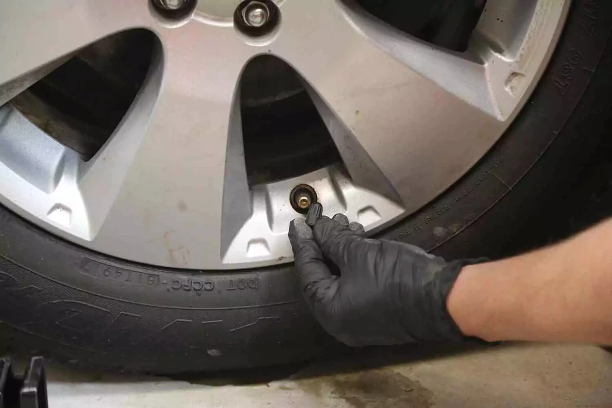 A mechanic wearing black gloves removes the cap from a tire's valve stem.