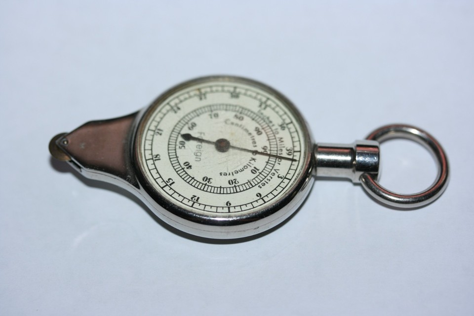 A vintage opisometer — a tiny wheeled instrument that traces map routes to calculate real-world distances — bundled with a compass, basically a spy gadget for cartography nerds.