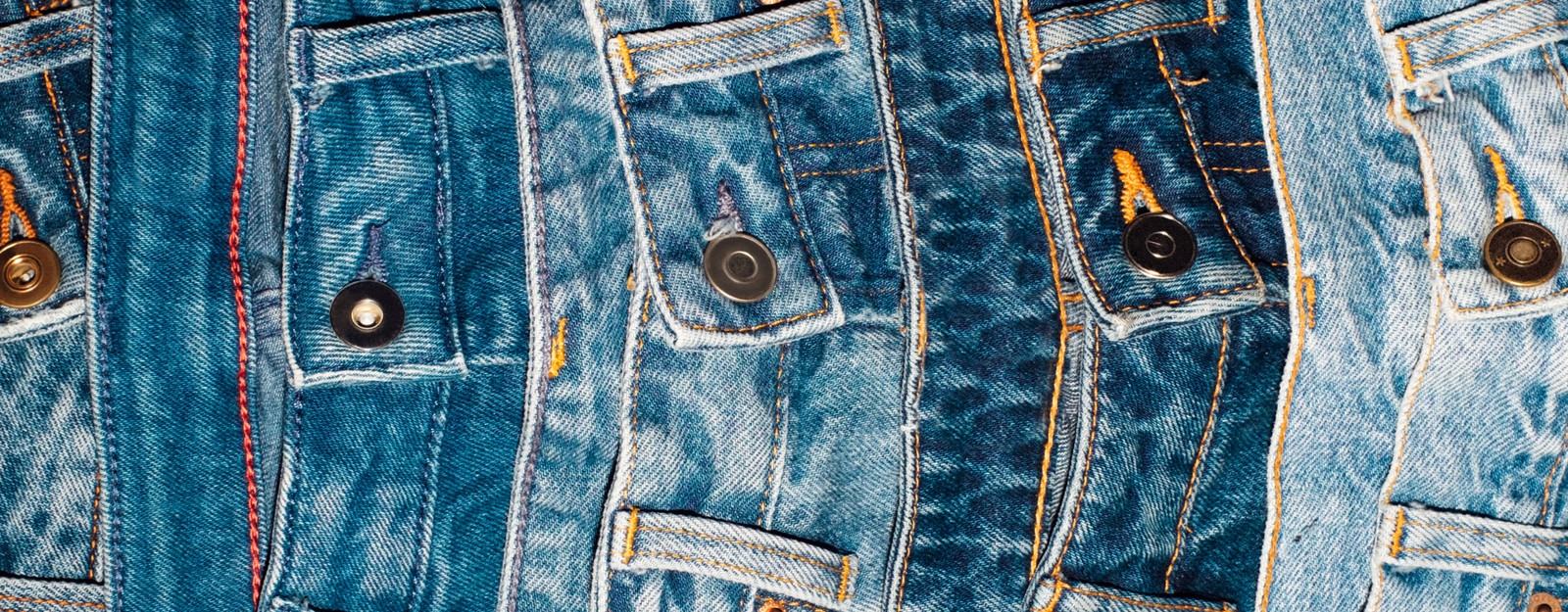 Eine Nahaufnahme mehrerer nebeneinanderliegender Jeanshosen in verschiedenen Blautönen.