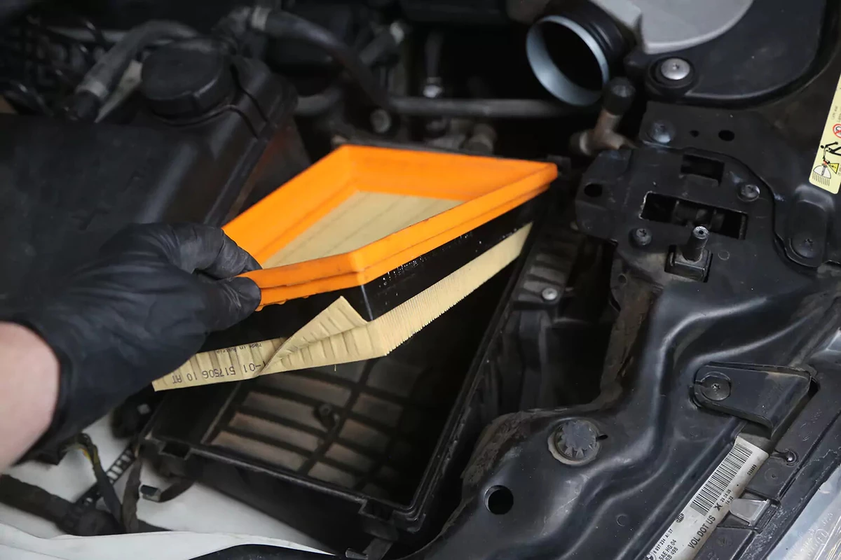 A mechanic wearing a black glove removes the air filter from the air filter box.