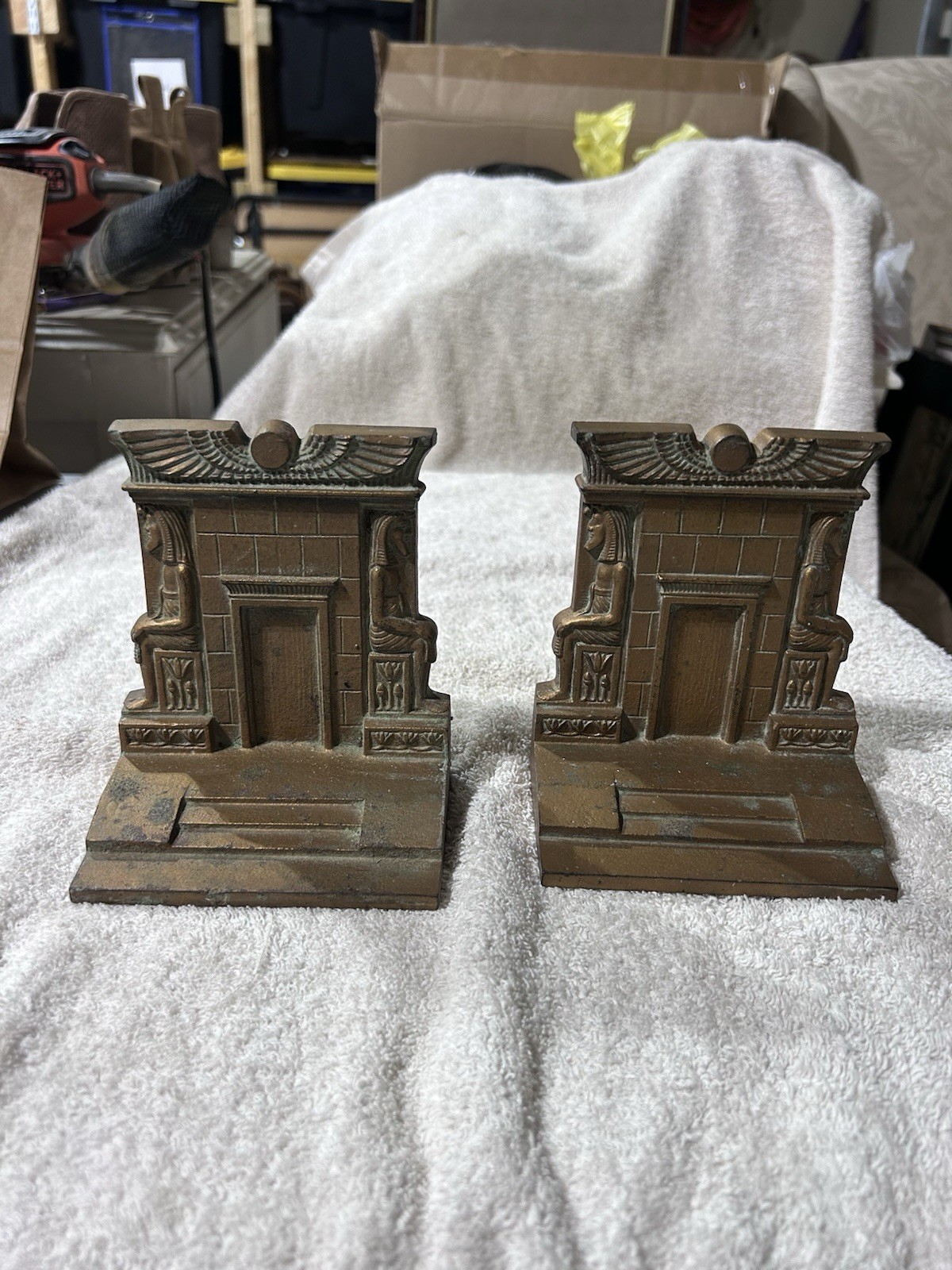 Pair of bronze-toned cast metal bookends shaped like ancient Egyptian temple facades with seated figures flanking a doorway beneath a winged sun disk.