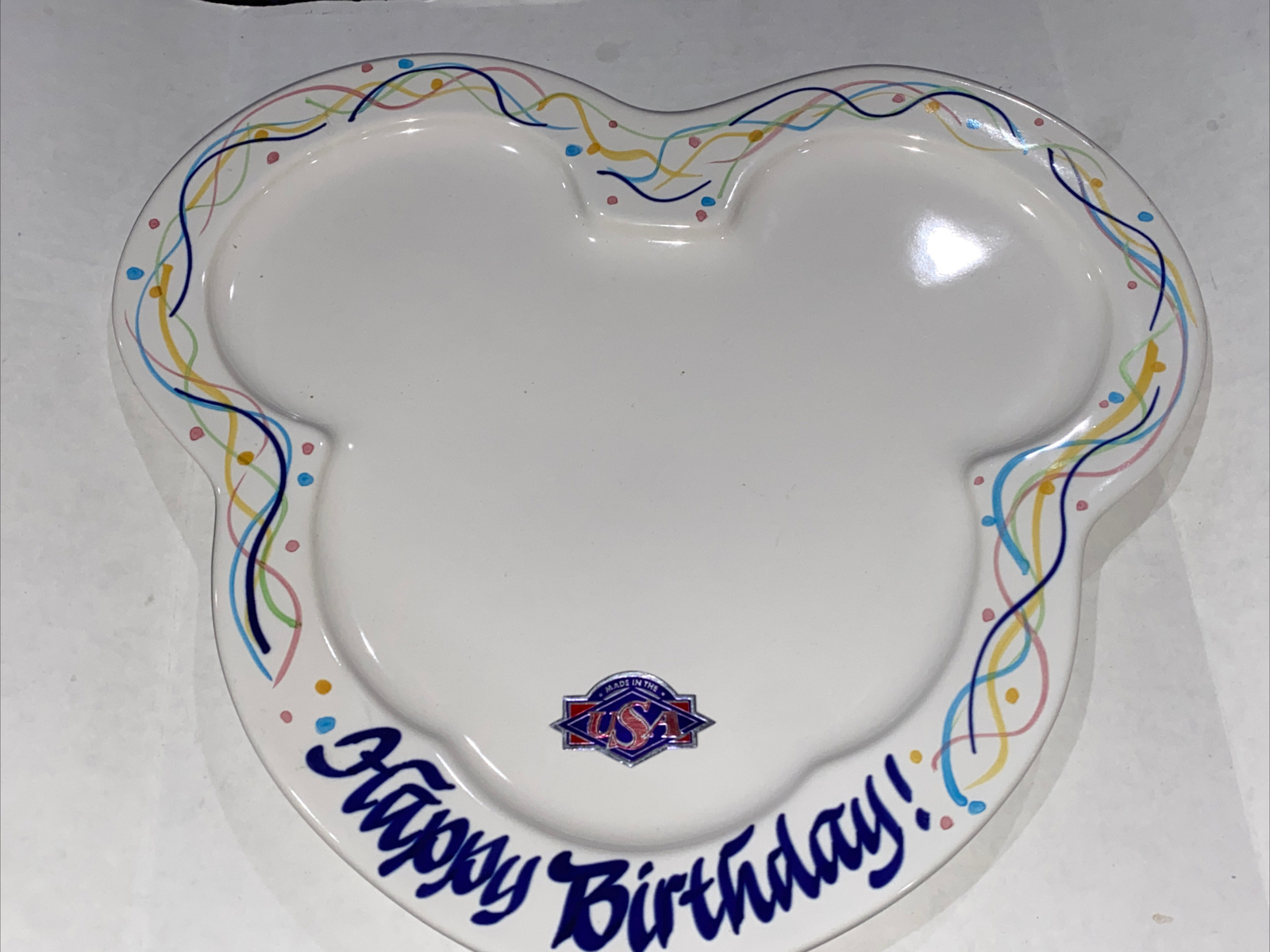 White Mickey Mouse shaped plate with “Happy Birthday!” text, colorful swirl border, and USA map design on the side.
