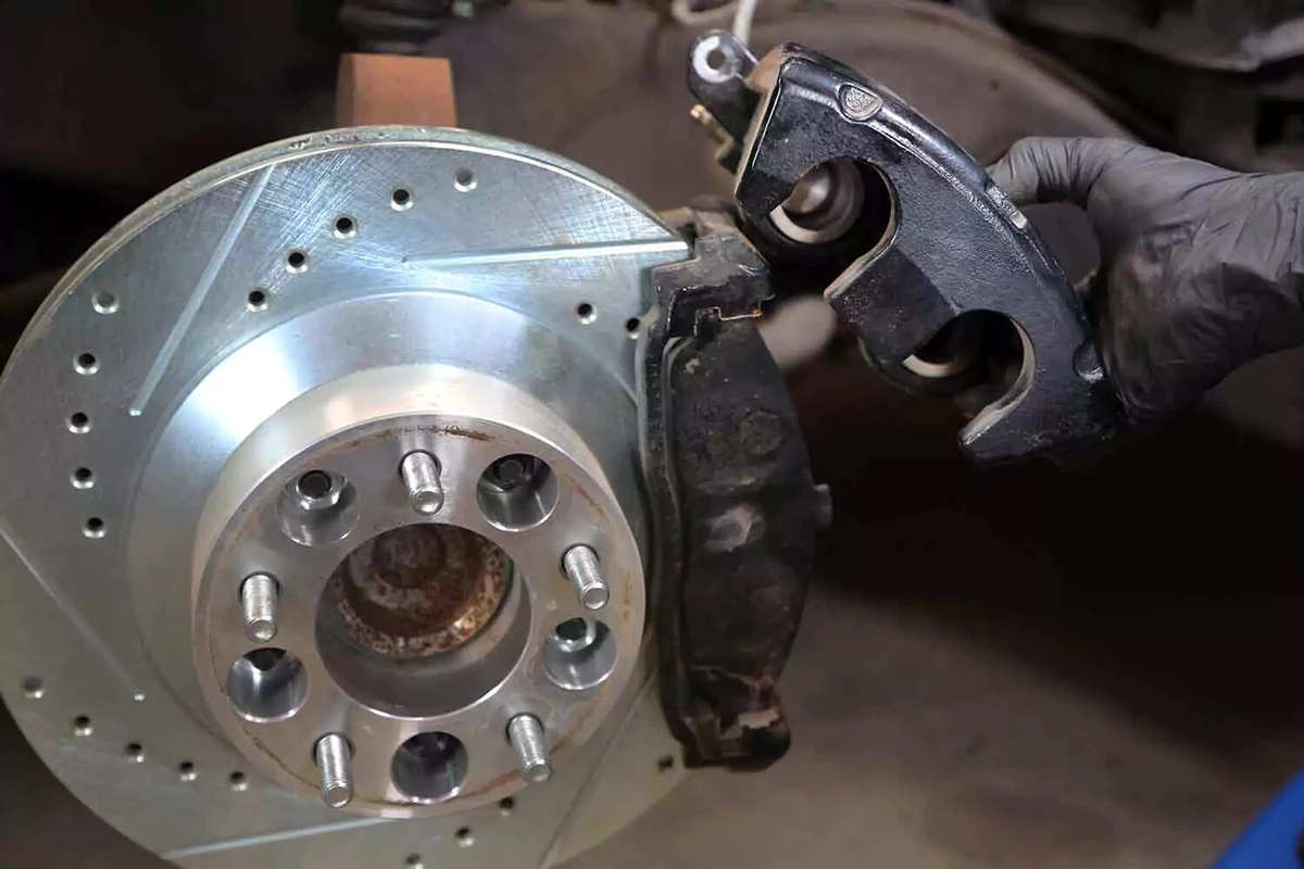 A mechanic pulling a brake caliper off its brake pads.