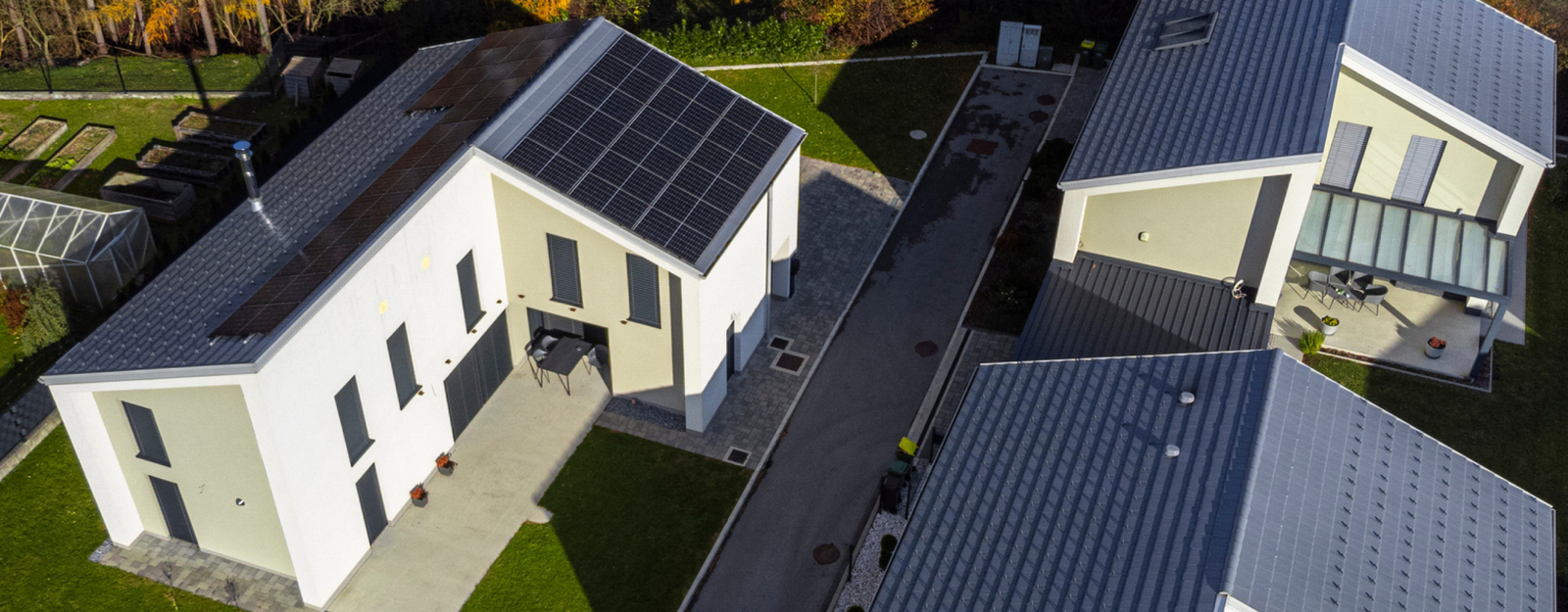 Drohnenaufnahme einer modernen Wohnanlage mit drei energieeffizienten Gebäuden, ausgestattet mit Solarpanelen auf den Dächern, umgeben von gepflegten Rasenflächen und einer herbstlichen Baumlandschaft.