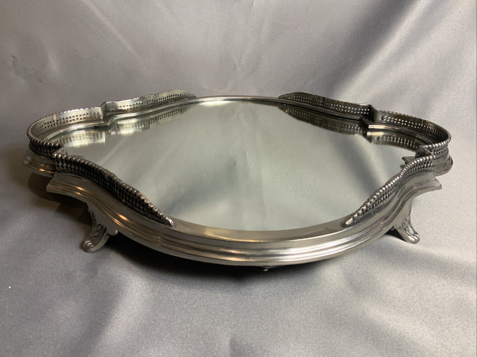 Oval mirrored serving tray with a pierced pewter gallery edge and scroll feet.