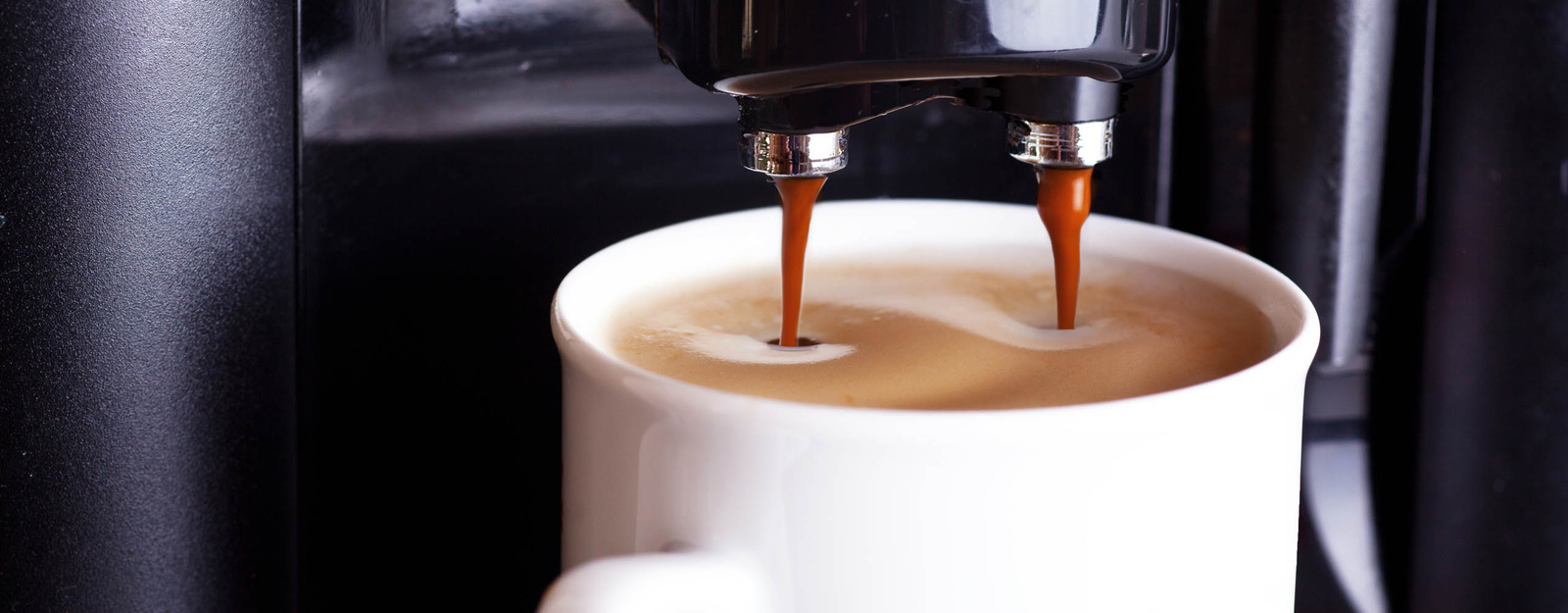 Eine Kaffeetasse aus Glas steht unter einem Kaffeevollautomaten und wird mit Kaffee gefüllt.