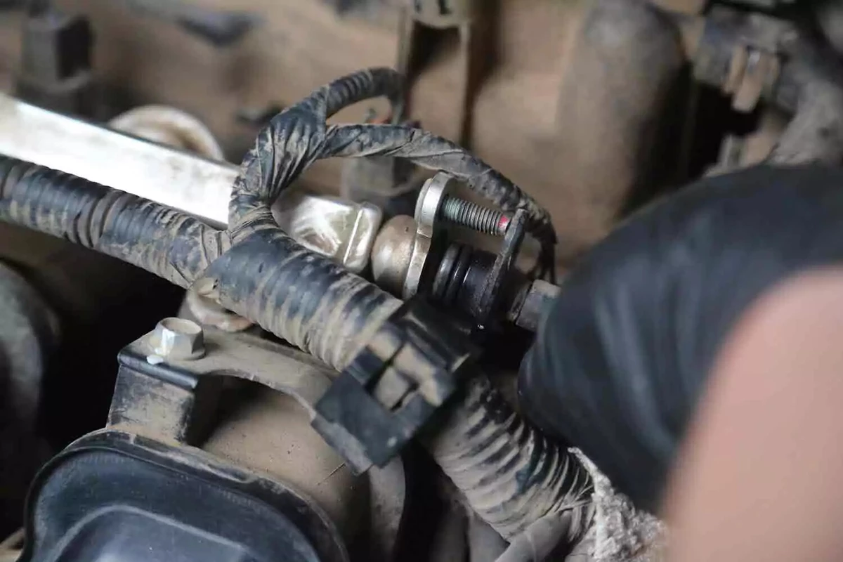 A mechanic wearing a black glove disconnects the fuel line.