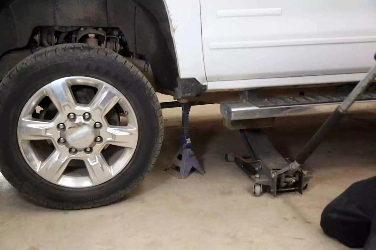 A mechanic using a floor jack to lower a pickup truck onto a jack stand.