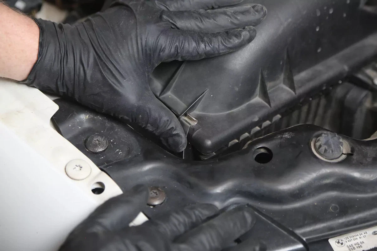 A mechanic wearing black gloves locks down the clips holding the lid on the engine air filter box.