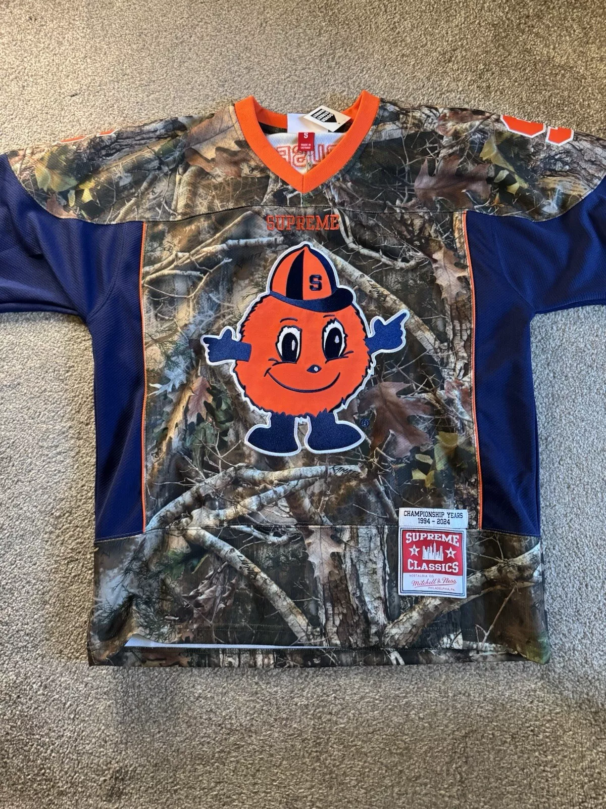 Maillot de hockey Supreme x Mitchell & Ness x NCAA camouflage orange moyen   en main