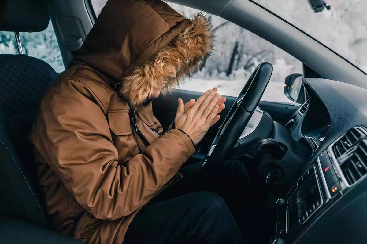 A driver wearing a parka warms his hands inside a cold car.