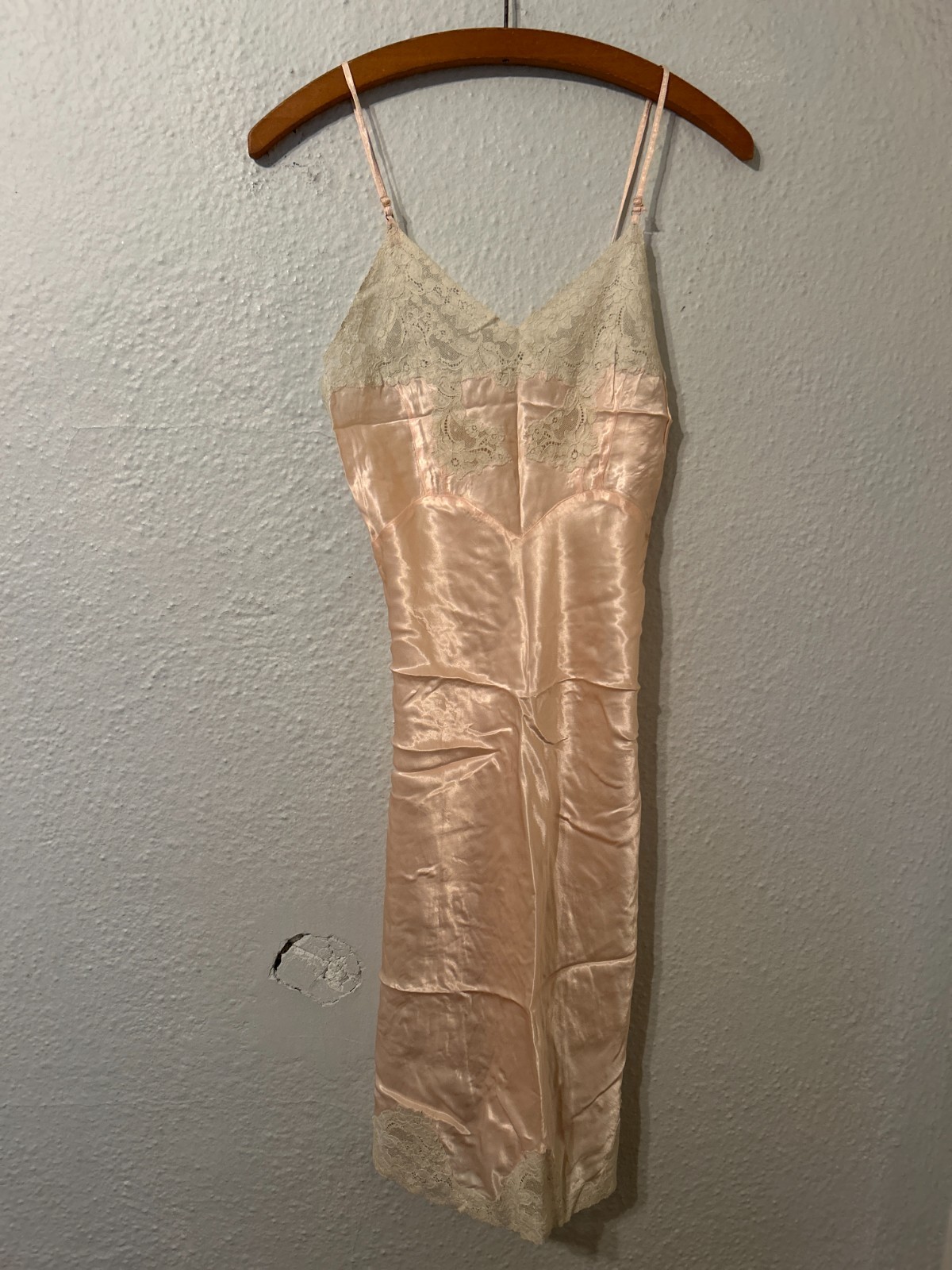 Pale pink satin slip dress with lace trim hanging on a wooden hanger
