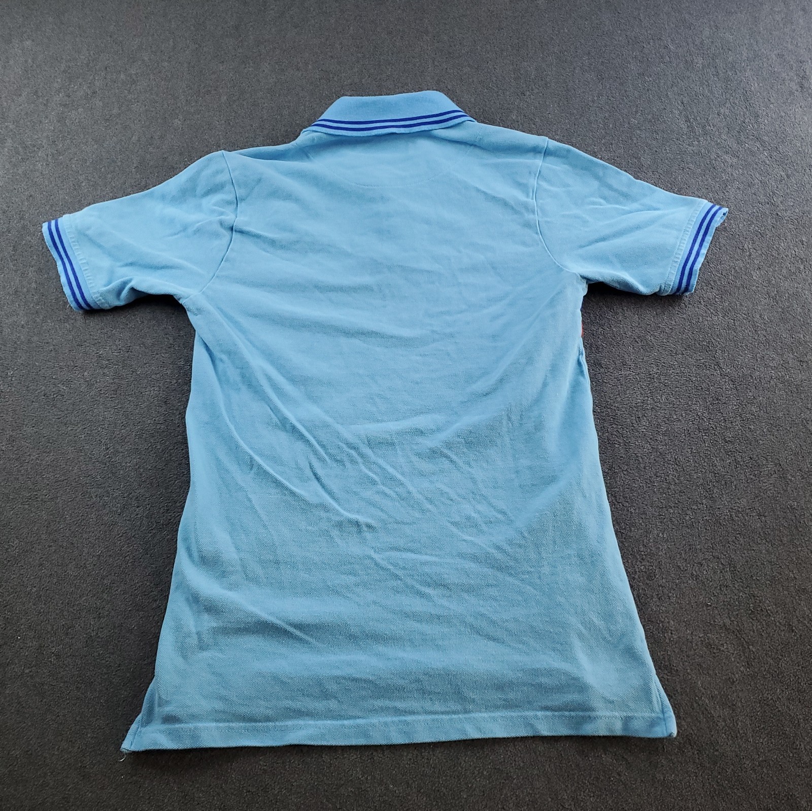 Light blue short-sleeve polo shirt with white sleeve trim, three-button placket, and blue Aston Martin logo on back.