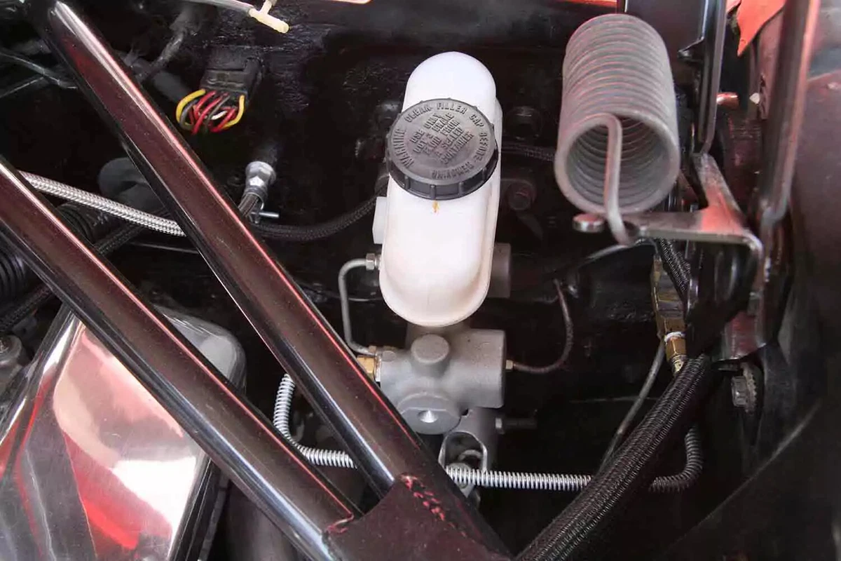 An aluminum brake master cylinder with a white plastic reservoir located under the hood of a vehicle.