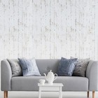 Off white metallic cracks lines faux distressed plaster wallpaper with textured floral pattern, displayed against a light gray sofa.