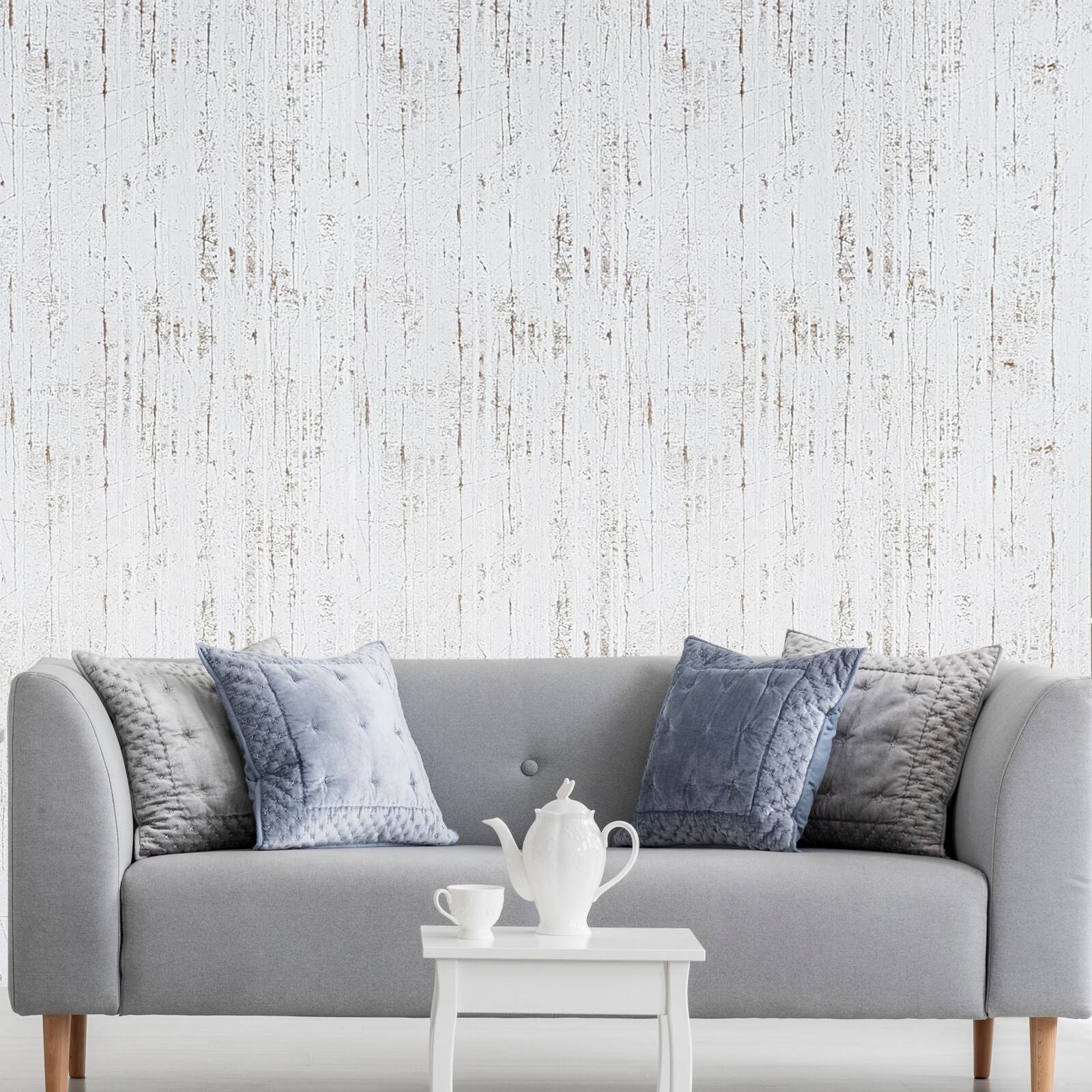 Off white metallic cracks lines faux distressed plaster wallpaper with textured floral pattern, displayed against a light gray sofa.