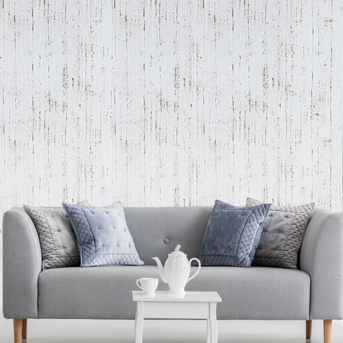 Off white metallic cracks lines faux distressed plaster wallpaper with textured floral pattern, displayed against a light gray sofa.