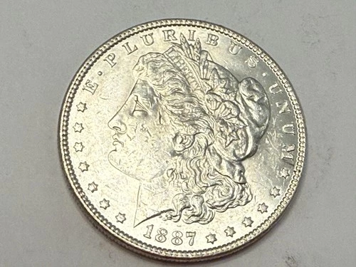 1887 Morgan U.S. silver dollar. Satiny white BU, bagmarks on jaw. #ek2