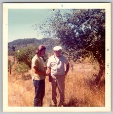 Vtg Color Snapshot Young Man And Older Man In Field With Large Tree Hills 1972