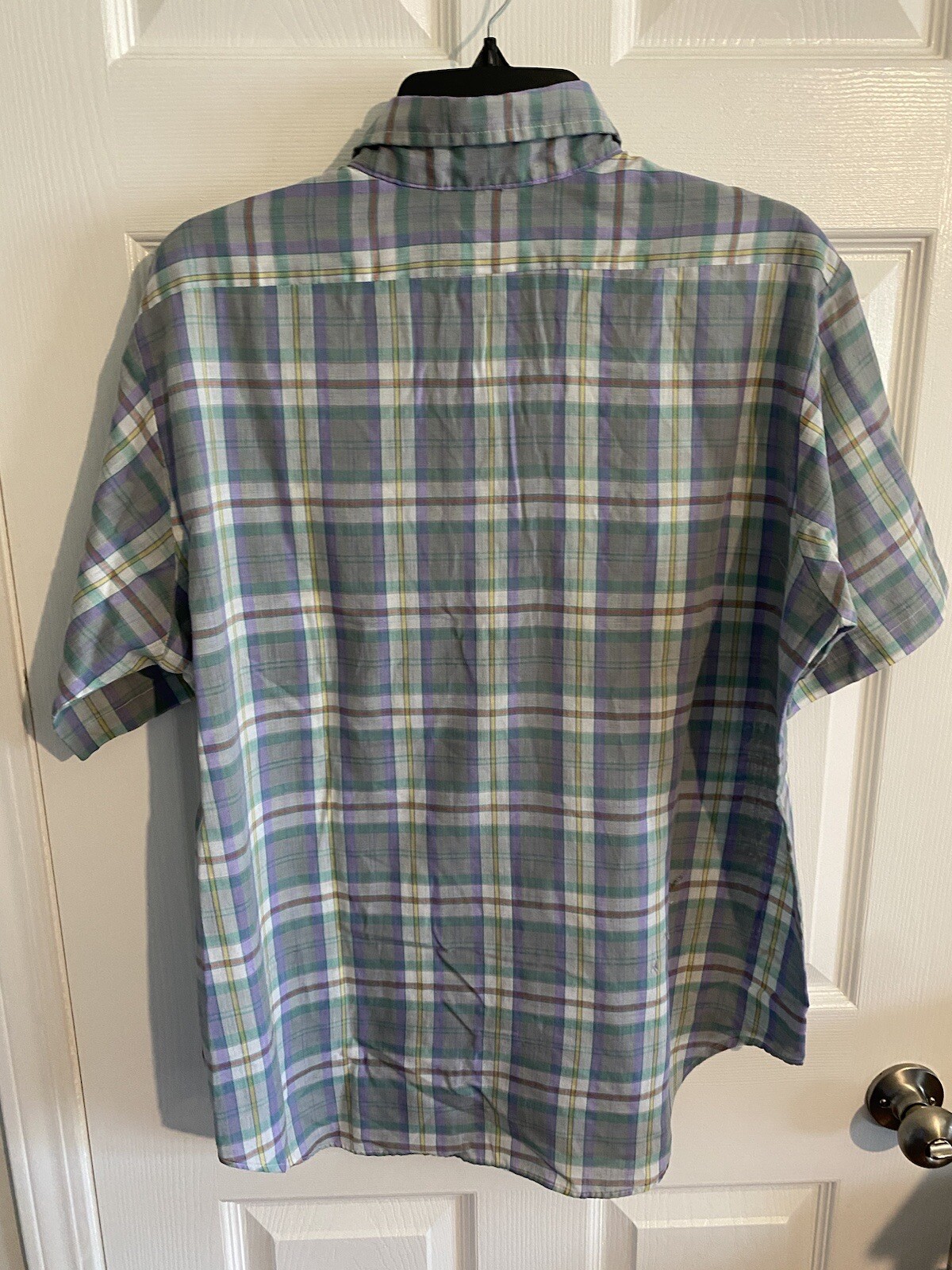 Men’s long-sleeve button-up shirt with green, blue, and yellow plaid pattern, hanging on black hanger against white door.