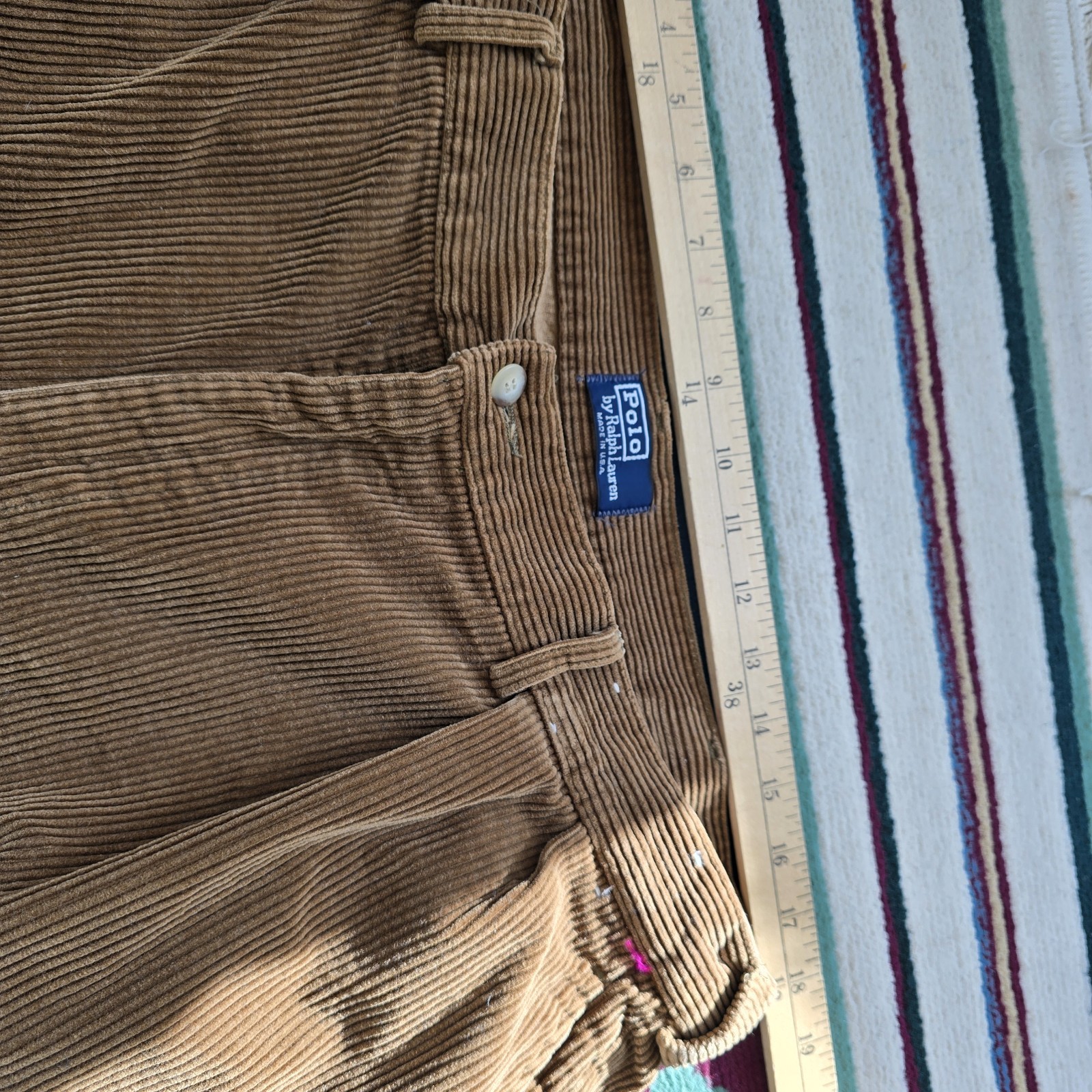 Brown corduroy pants with white Polo Ralph Lauren label, button closure, and straight hem, laid flat beside a 12-inch ruler.