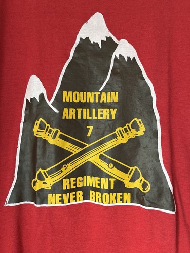 Red vintage 80s army shirt with yellow mountain graphic and text “Mountain Artillery Regiment Never Broken” in bold yellow letters.