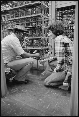 African American man and a woman working on telephone apparatus indoors 1979