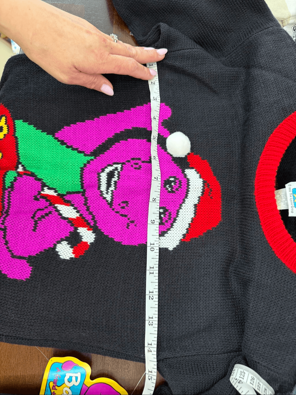 Black knit sweater with pink and green cartoon Barney face graphic, white snowflakes, and “Made in USA” text.