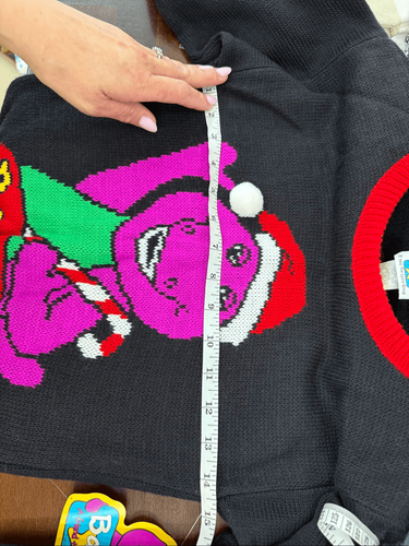 Black knit sweater with pink and green cartoon Barney face graphic, white snowflakes, and “Made in USA” text.