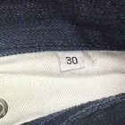 White fabric tag on inner waistband of Gustin jeans, marked “30x29 indigo raw selvedge” with black text.