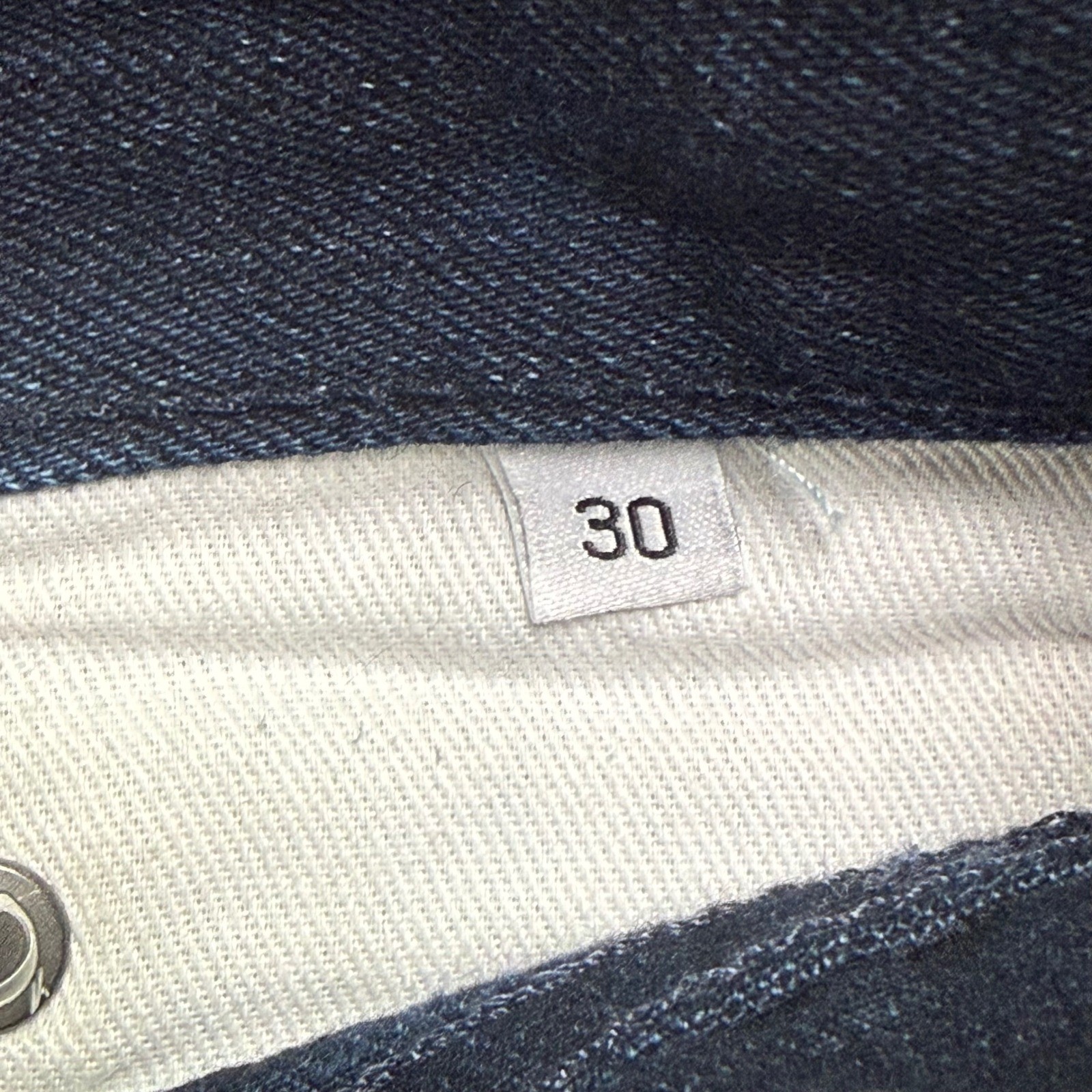 White fabric tag on inner waistband of Gustin jeans, marked “30x29 indigo raw selvedge” with black text.