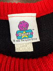 White fabric tag on red knit sweater with purple Barney graphic, blue “Barney” text, and red-yellow care instructions.