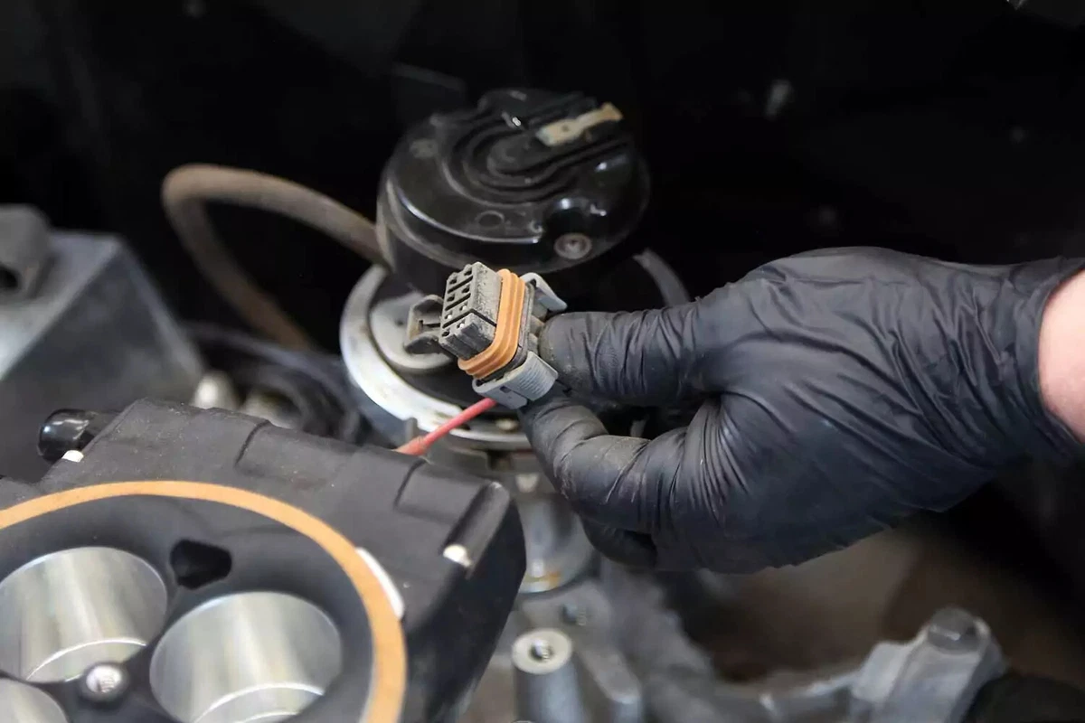 A mechanic removes the distributor’s wiring plug.